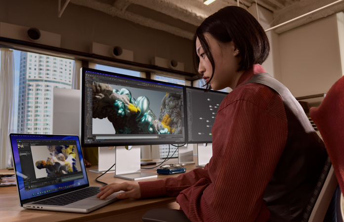 Osoba v kanceláři pracuje na MacBooku Pro připojeném ke Studio Displayi XDR