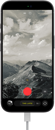 iPhone 18 Pro, μπροστινή εξωτερική όψη που δείχνει ένα ορεινό τοπίο, με επικάλυψη της λειτουργίας κάμερας στη λειτουργία Time-Lapse, με καλώδιο τροφοδοσίας συνδεδεμένο στη θύρα φόρτισης