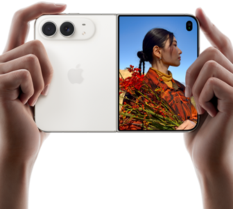 „iPhone Duo“, žvaigždžių baltos spalvos, horizontalioje padėtyje, atlenktas, kairiajame skydelyje matomos 48 MP „Dual Fusion“ galinės kameros, dešiniajame skydelyje matomas žmogus, kurio nuotrauka daroma iš išorinio ekrano, fotografuojamas asmuo gali matyti savo veidą, kol daroma nuotrauka naudojant „Duo Preview“