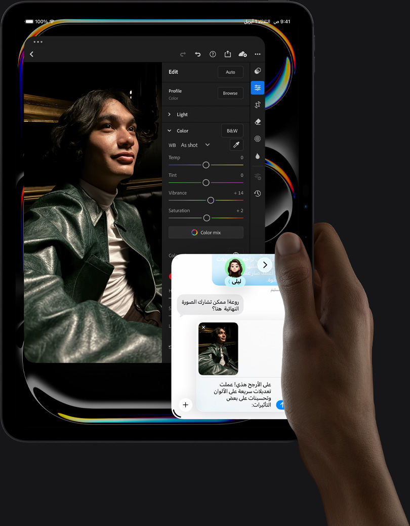 جهاز iPad Pro، الجزء الأمامي الخارجي، الوضع العمودي، لون أسود فلكي، يد يمنى تحمل الجهاز، شاشة تعرض تطبيقاً لتعديل الصور مع صورة لشخص يرتدي زياً أزرق، وأدوات التعديل وخياراته في القائمة اليمنى، وفي الجزء السفلي الأيمن من الشاشة تبدو محادثة iMessage جارية بين المستخدم وشخص آخر لمراجعة الصورة