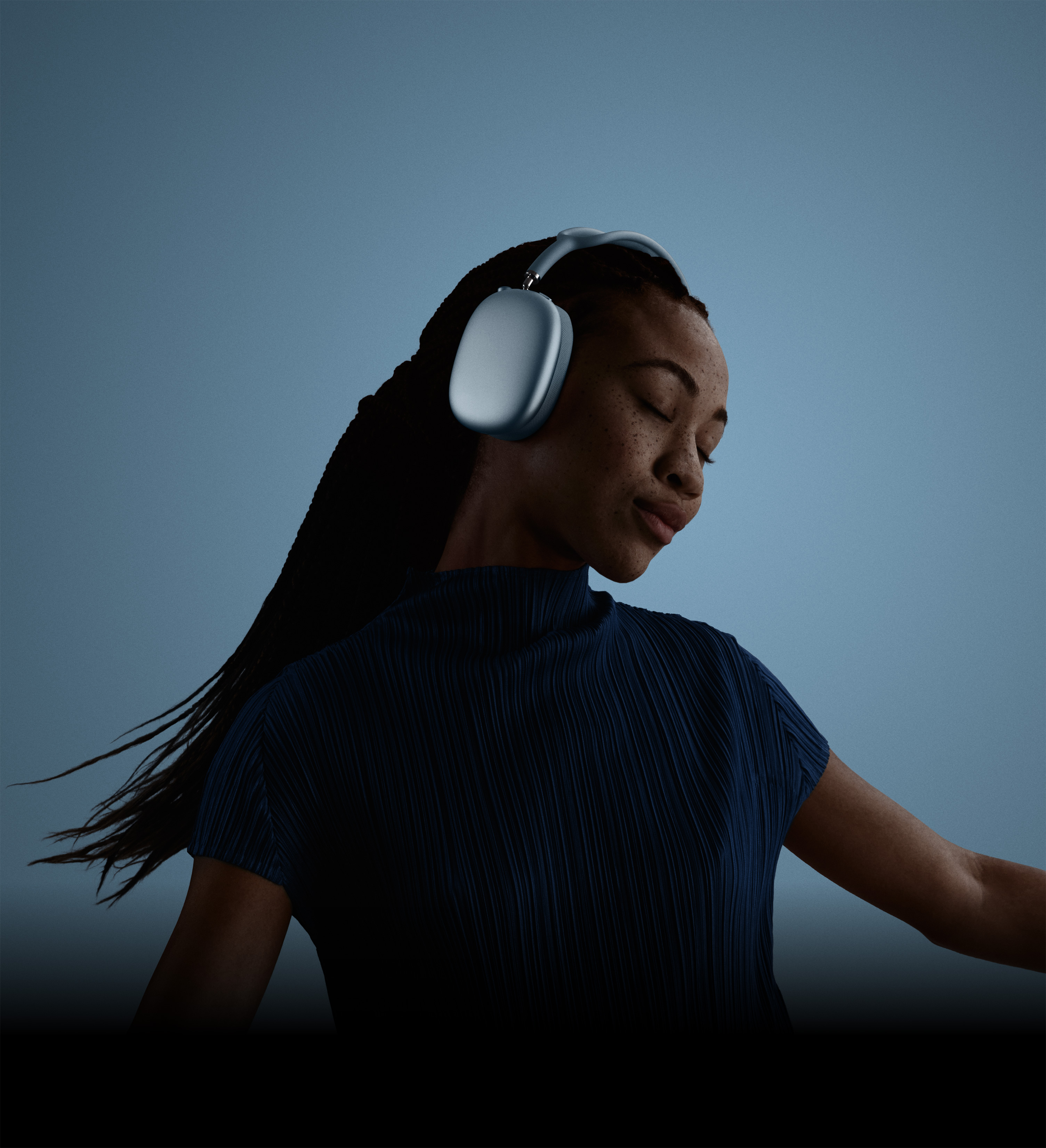 A person with eyes closed and head tilted, side profile, wearing AirPods Max 2 headphones in blue color.
