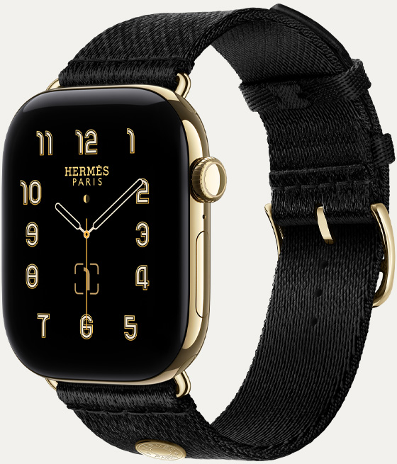 Apple Watch Hermès Series 12, esfera analógica Clou de Selle (aguja horaria, minutero y segundero, complicaciones: fase lunar, fecha), caja de titanio, color oro brillante, lateral derecho, Digital Crown, botón lateral, con la correa Clou de Selle Satin, color Noir, en suave tejido de satén negro con componentes en oro brillante a juego con la caja del reloj