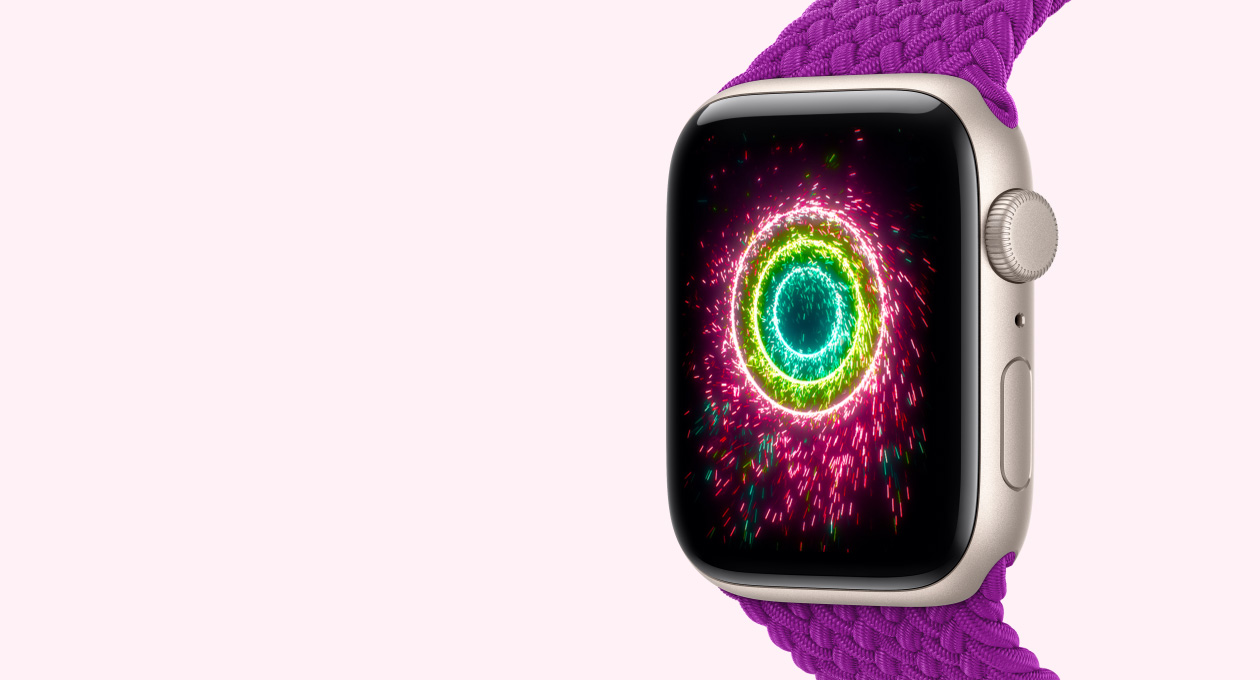 Apple Watch SE 3, Aluminiumgehäuse in Polarstern mit Geflochtenem Solo Loop Armband in Magenta, das Display zeigt Aktivitätsringe, die als Wunderkerzen gestaltet sind, konzentrische Ringe in Pink, Limettengrün und Hellblau