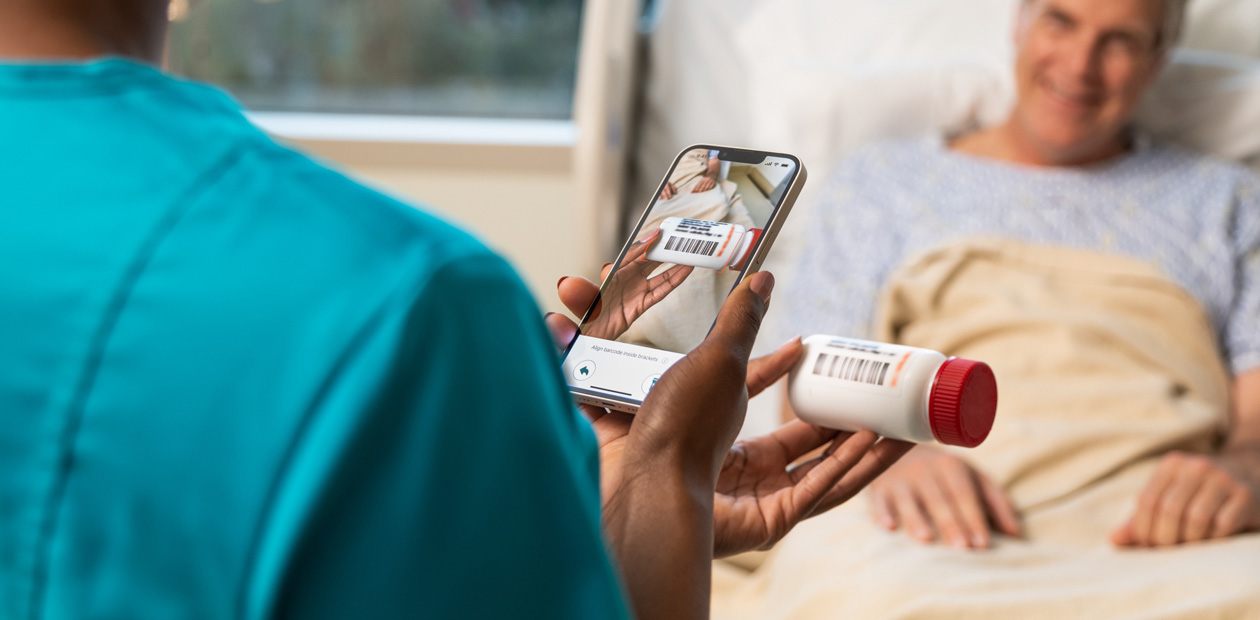 Eine Pflegekraft im blaugrünen OP‑Kittel scannt die Medikamente für Patient:innen mit ihrem iPhone.