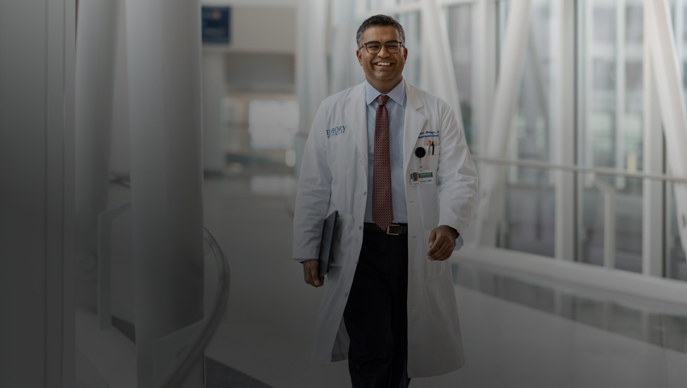 Un médico camina con un MacBook bajo el brazo derecho.