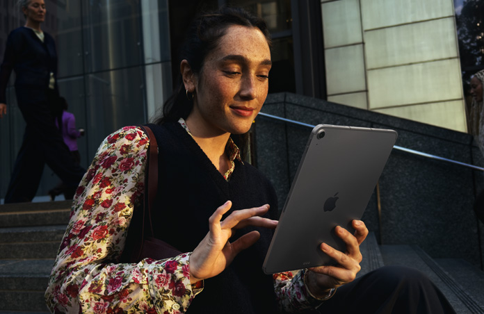 Iemand die buiten op de trap van een groot gebouw zit met een 11-inch iPad Air in Spacegrijs blijft naadloos verbonden met wifi terwijl er van netwerk wordt gewisseld