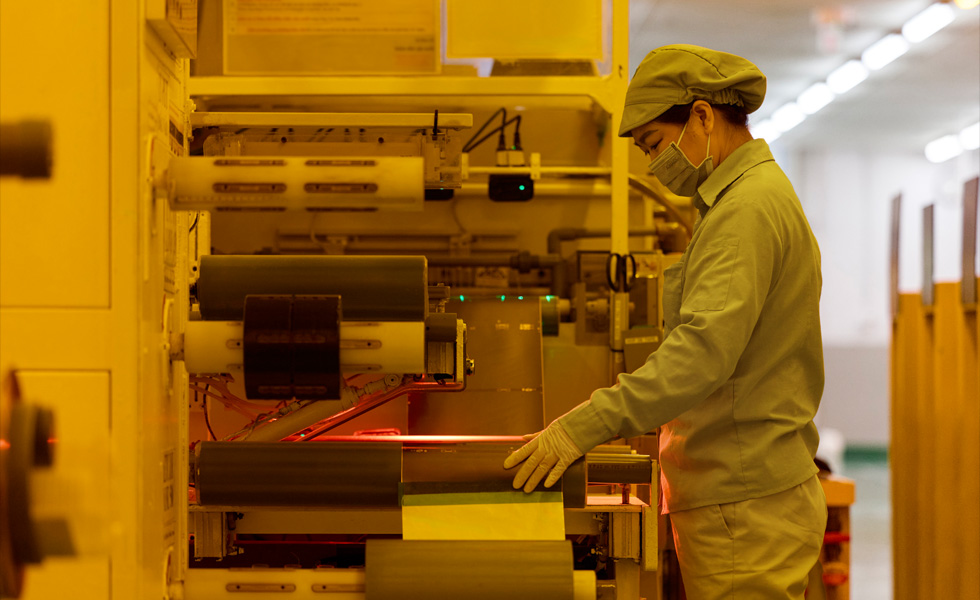 A uniformed employee with a face mask presses buttons on a piece of manufacturing equipment