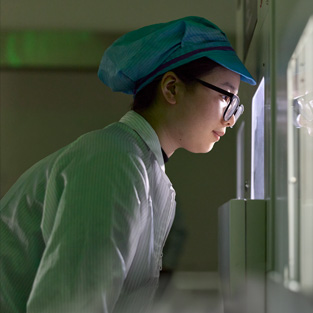 An employee in full-coverage work suit and eye wear observes Apple Watch assembly